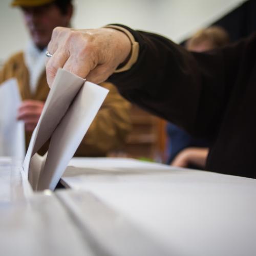 Image of a persons hand submitting a polling card into a box