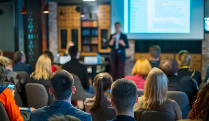 Image of a presenter, speaking at a workshop in front of a crowd.