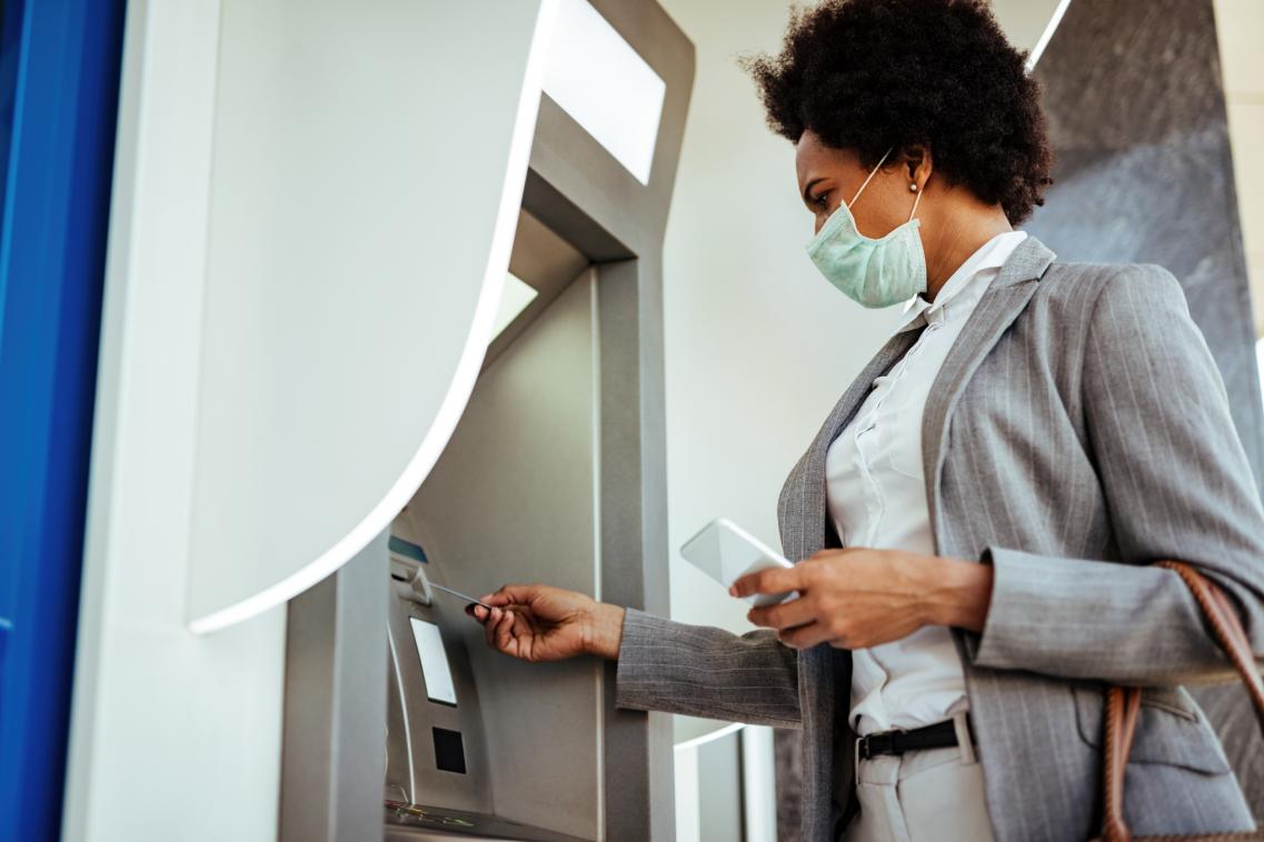 An image of a woman in a mask using an ATM