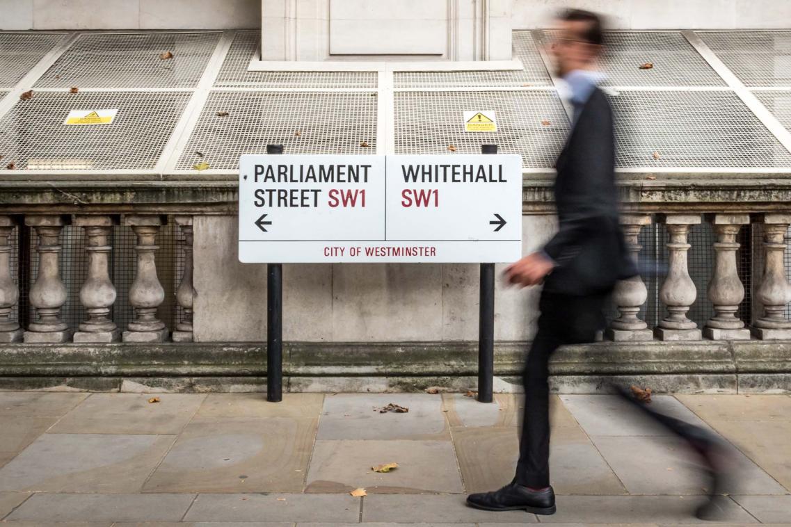 Suited man walks past signs to UK Parliament