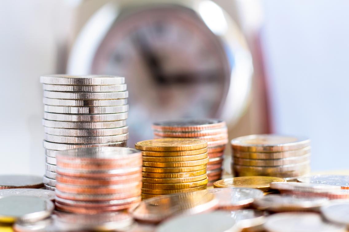 An image showing piles of coins at different heights with a clock in the background