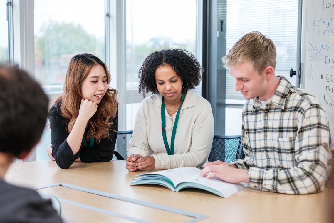 Image of three people sitting at a table sharing a book to look at