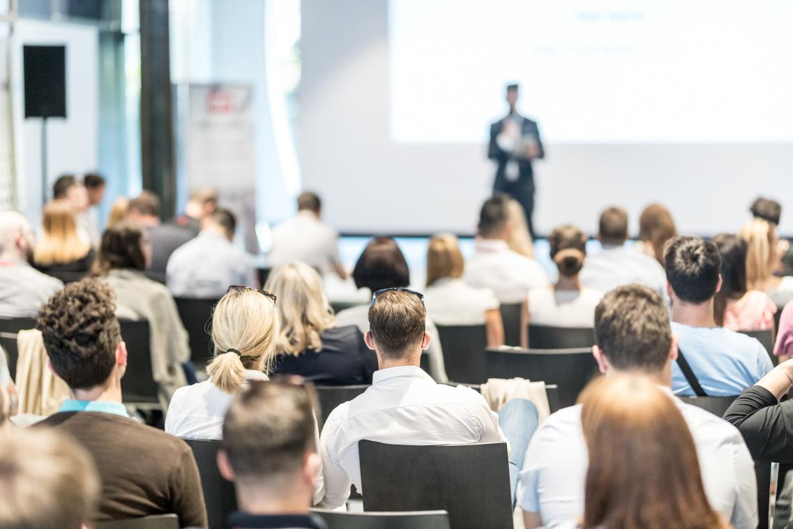 Image of people sitting at a conference facing the stage