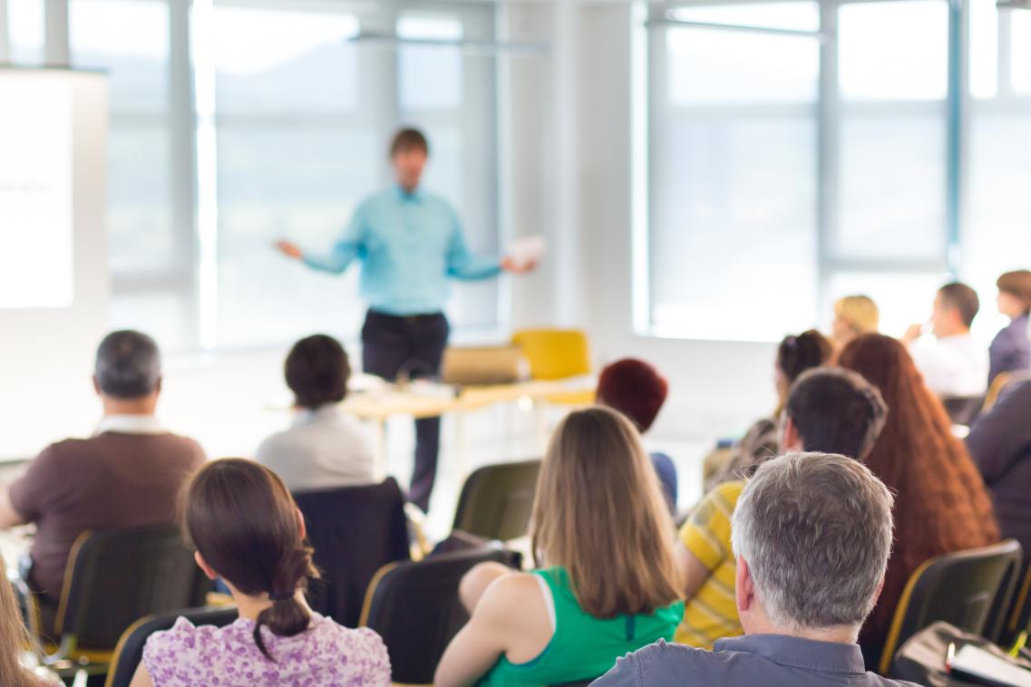 Image from back of the room at a workshop with a person speaking to the audience