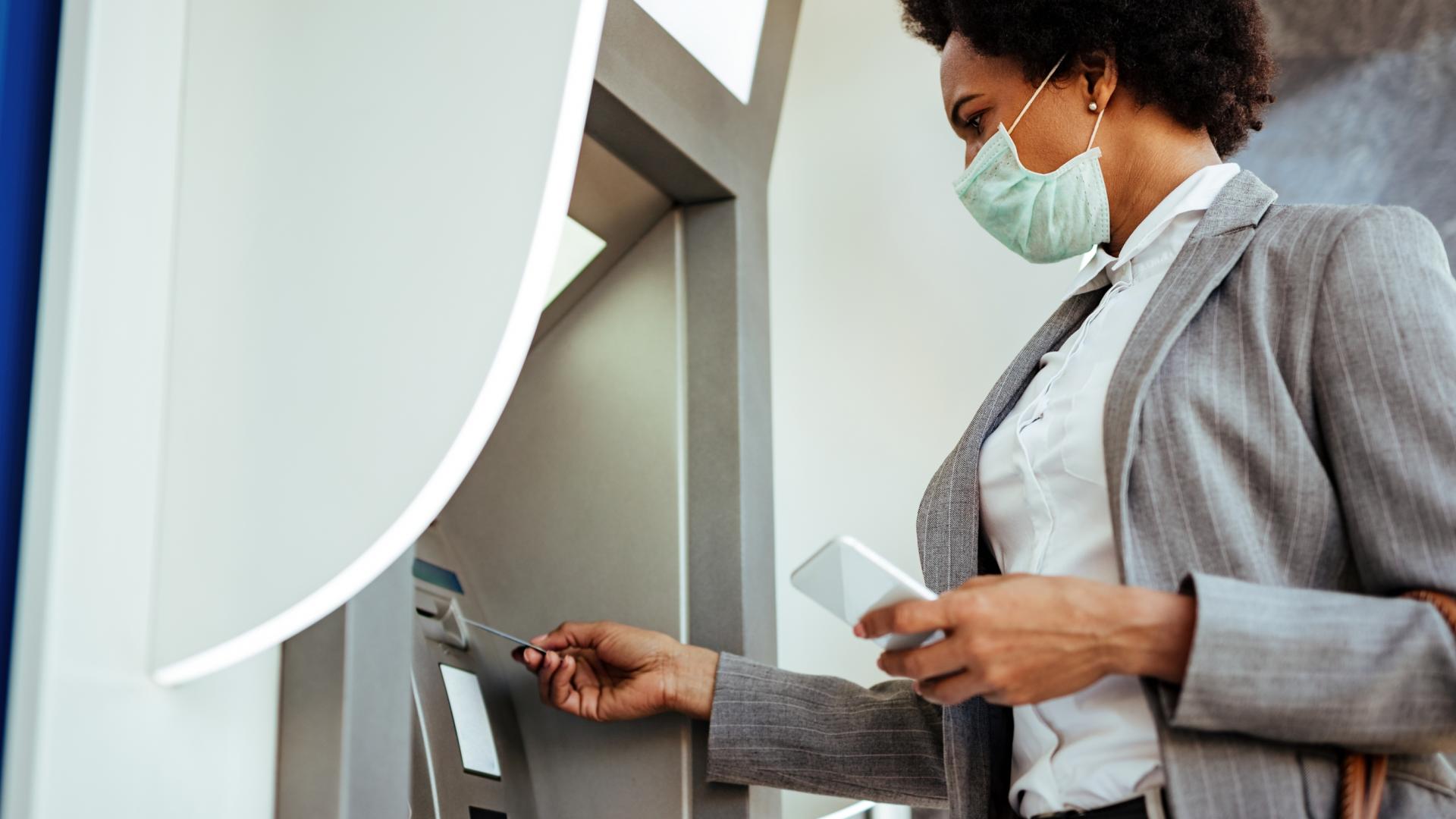 An image of a woman in a mask using an ATM