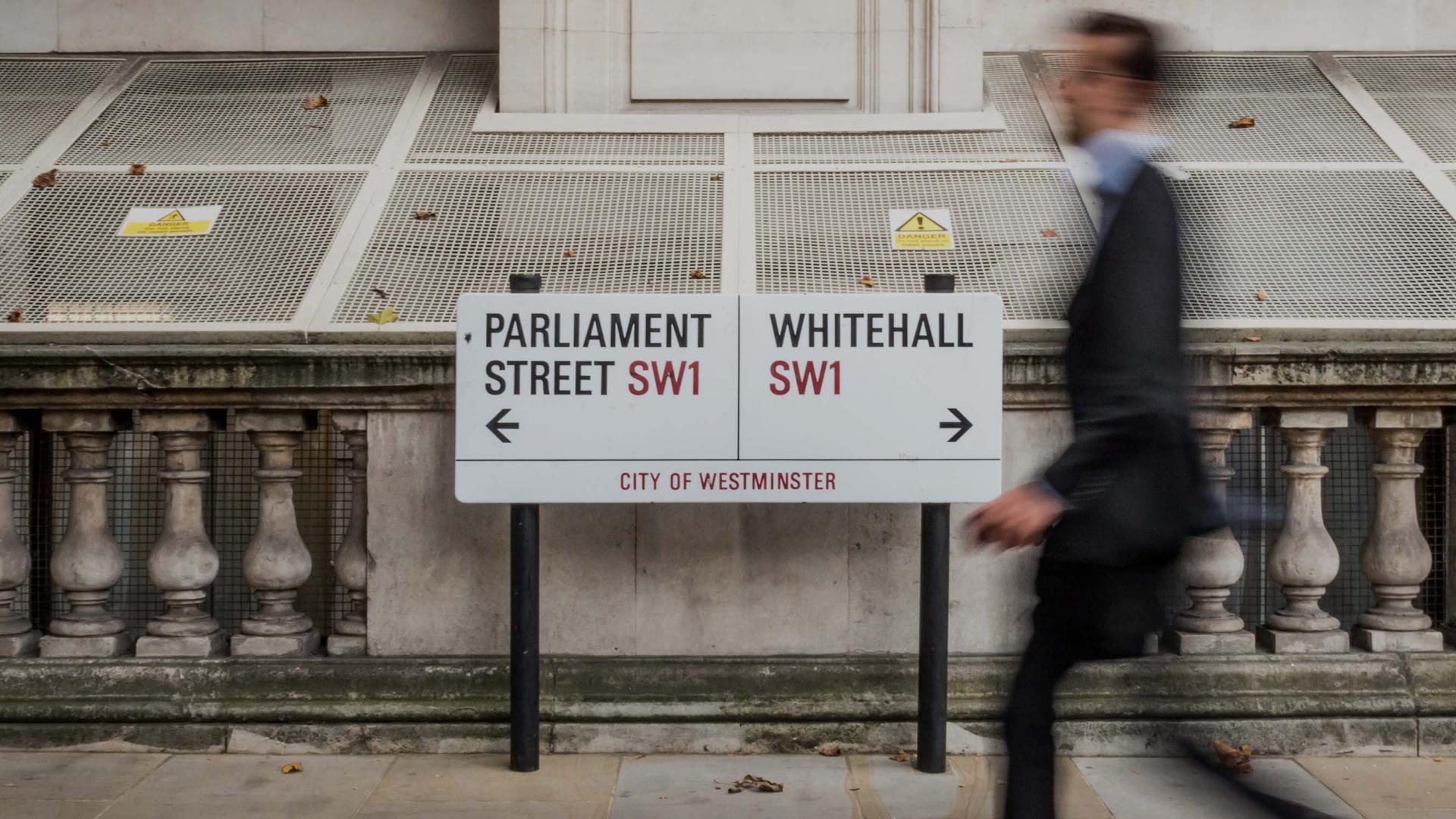 Suited man walks past signs to UK Parliament