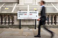 Suited man walks past signs to UK Parliament