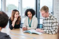 Image of three people sitting at a table sharing a book to look at