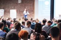 Image of people at a conference listening to the speaker providing lecture on scene in big conference hall.