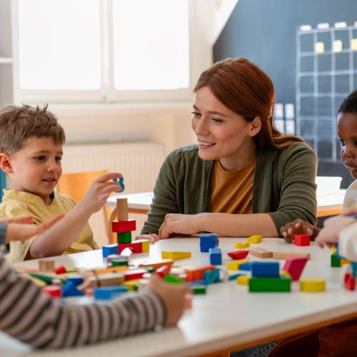 Pre-school children sitting at a table playing with building blocks with a teacher