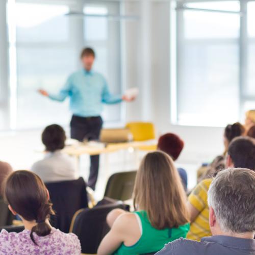 Image from back of the room at a workshop with a person speaking to the audience